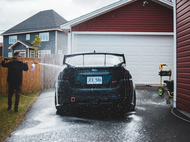 Worker pressure washing a car in a driveway