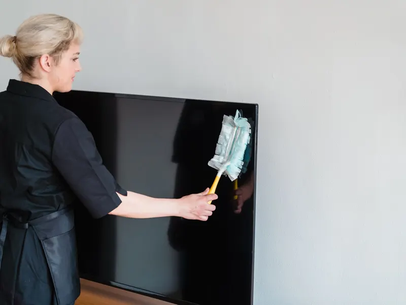 Cleaner dusting a large flat-screen TV