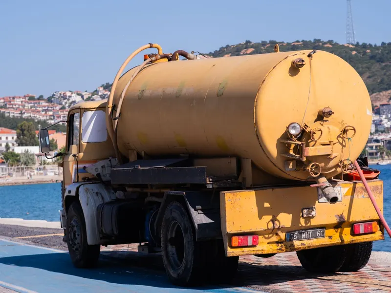 Yellow septic tanker truck parked by the water